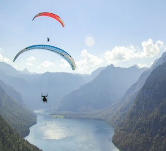 Two paragliders flying over an alpine lake and mountains in Austria