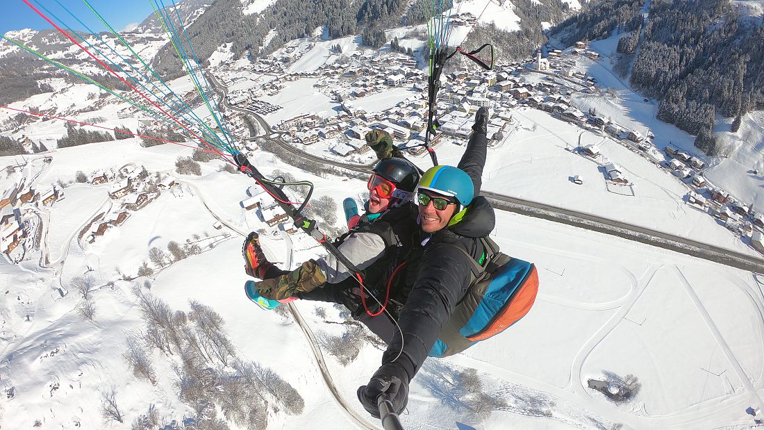 Tandem paragliding in Grossarl, Austria with winter views over a snow-covered village and alpine valley landscape.