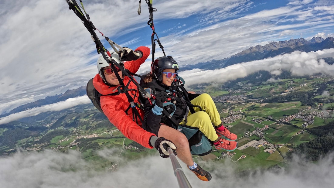 Tandem paragliding in South Tyrol, Italy with sweeping alpine views over green valleys, villages, and distant mountain peaks.