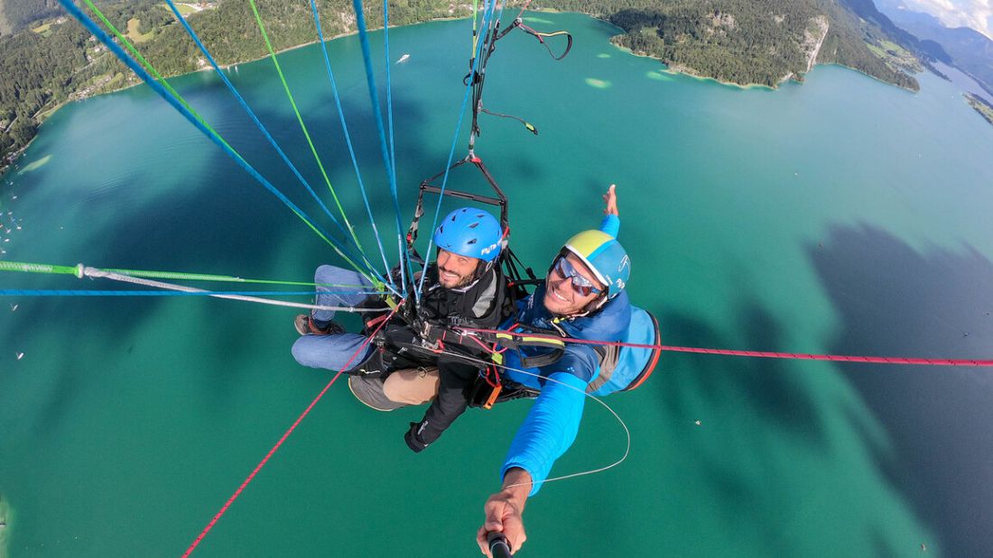 Tandem paragliding over Wolfgangsee near St. Gilgen, Austria with turquoise lake views and surrounding mountains.