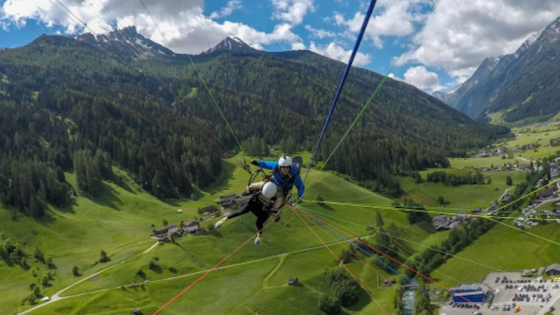 Tandem paragliding in the Stubai Valley near Innsbruck, Austria with sweeping alpine meadows, forests, and mountain views below.
