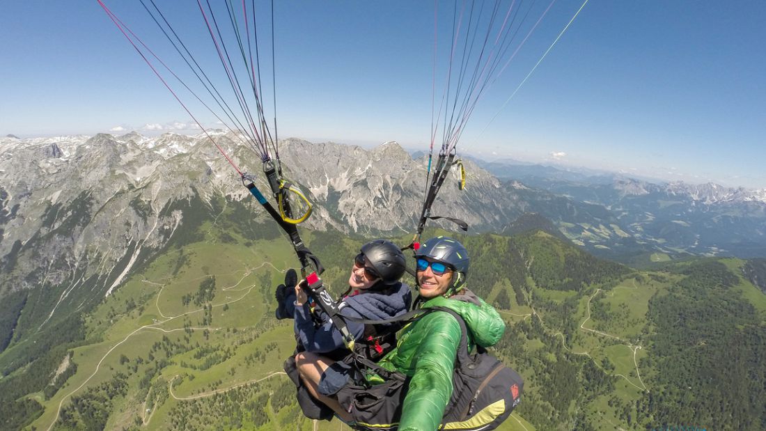 Tandem paragliding in Werfenweng, Austria with panoramic alpine mountain views and green valleys below.